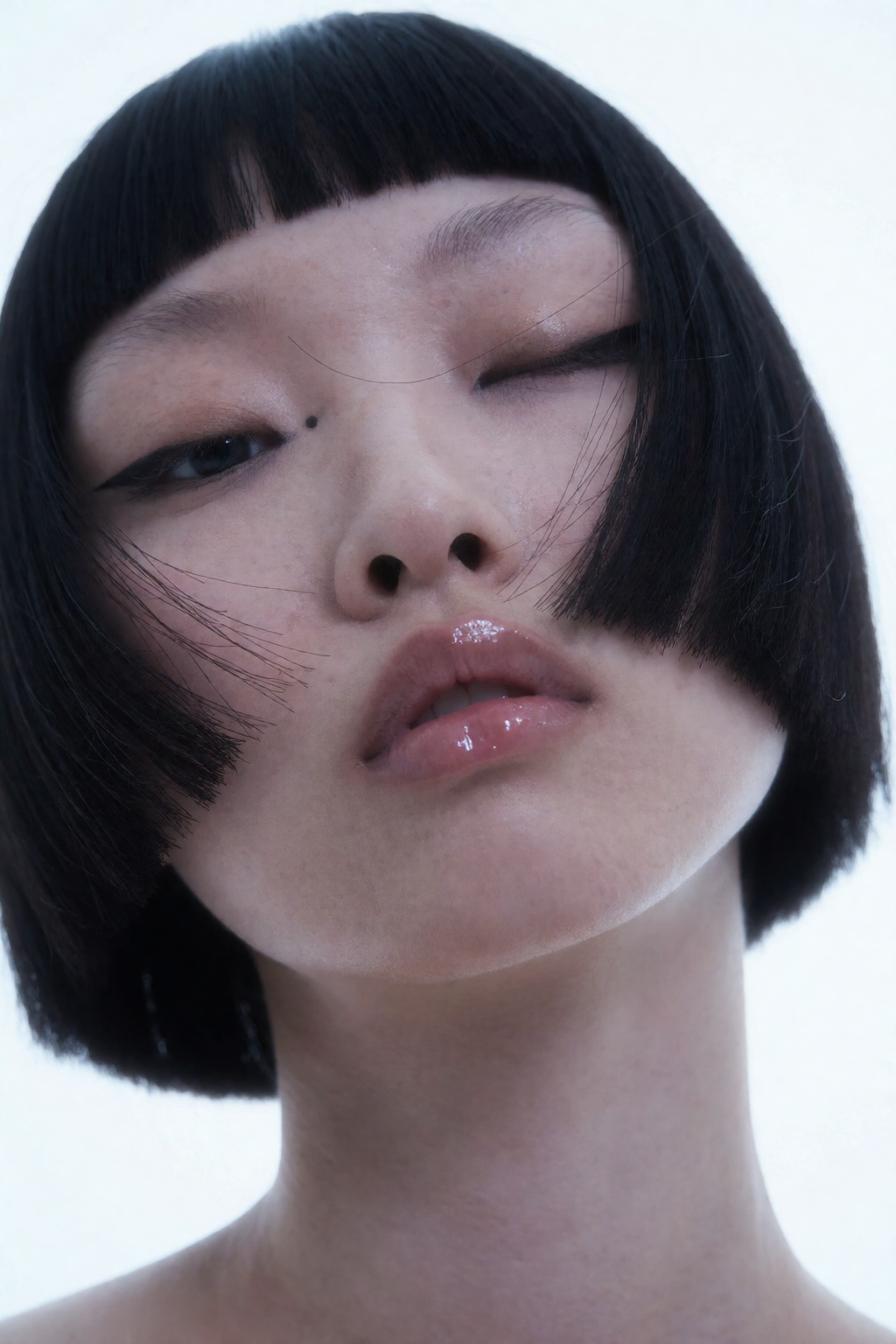 A low-angle extreme close-up portrait of an East Asian model with a sharp geometric black bob haircut against a luminous w...