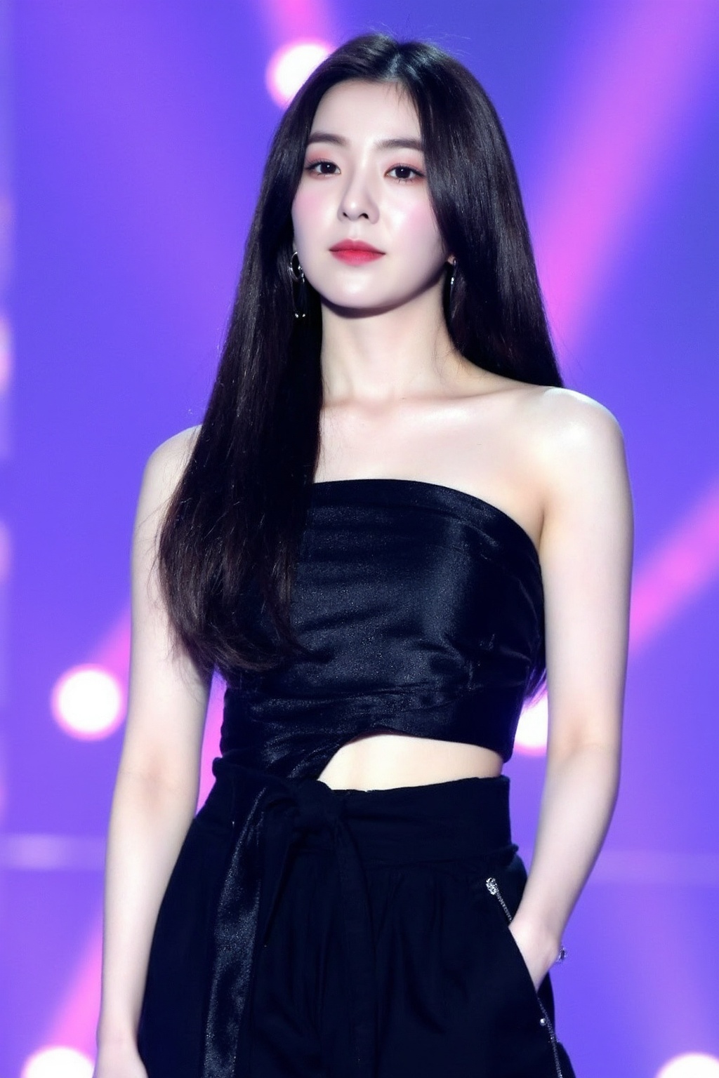 The image shows a young korean woman singing on stage. She has long,  dark hair and is wearing a fitted,  strapless black...