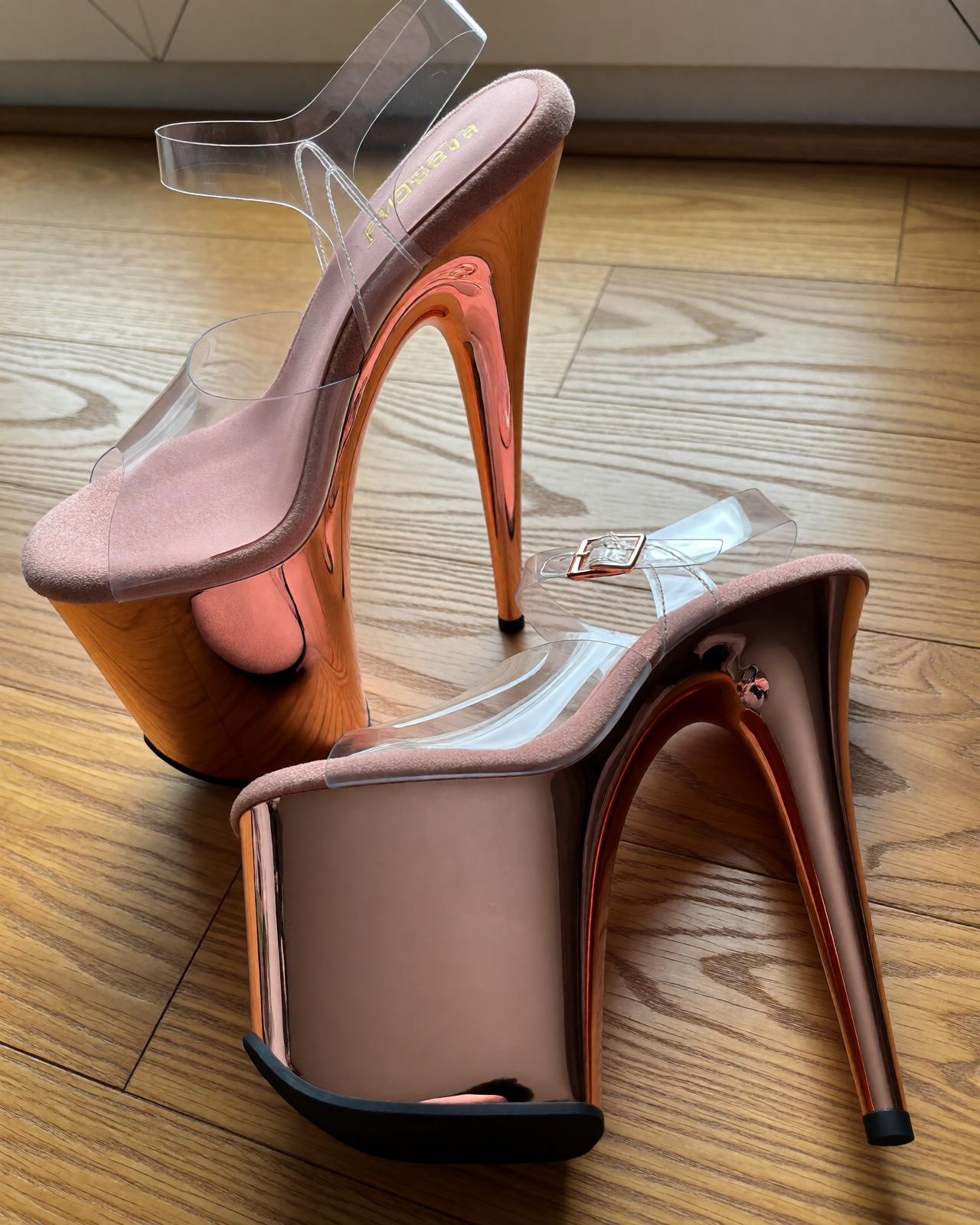 A detailed product photograph of rose-gold brushed metallic Pleasers Flamingo extreme platform heels on warm light oak flo...
