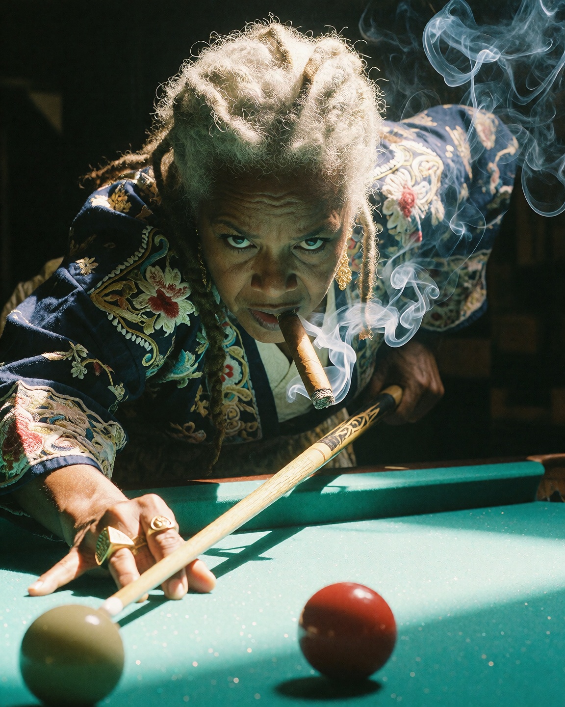 An older Black woman with silver dreadlocks in a heavily embroidered indigo kimono leans intently over a brightly lit gree...