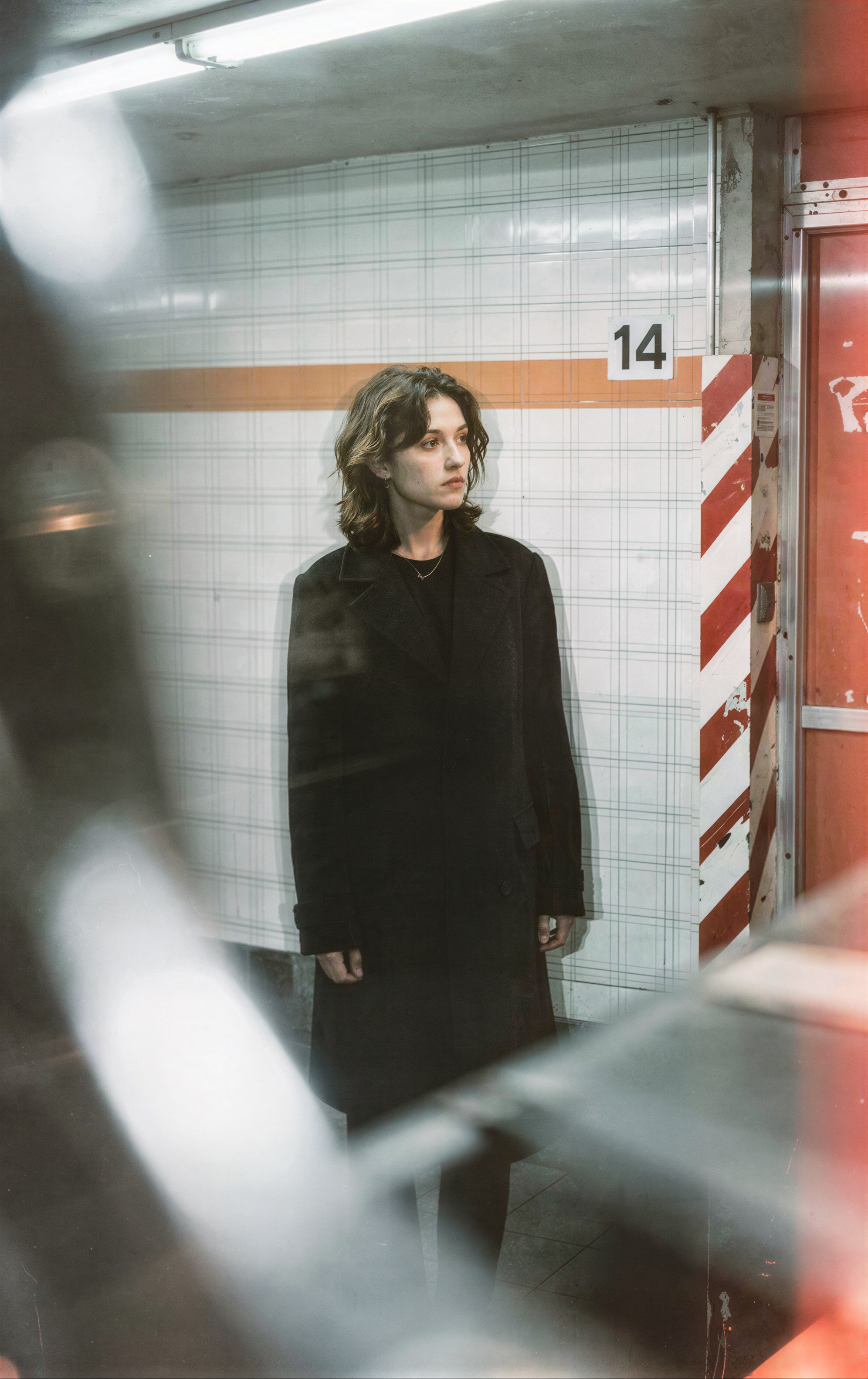 photograph of a young woman with light brown,  shoulder-length hair standing in a dimly lit,  tiled subway station on Tens...
