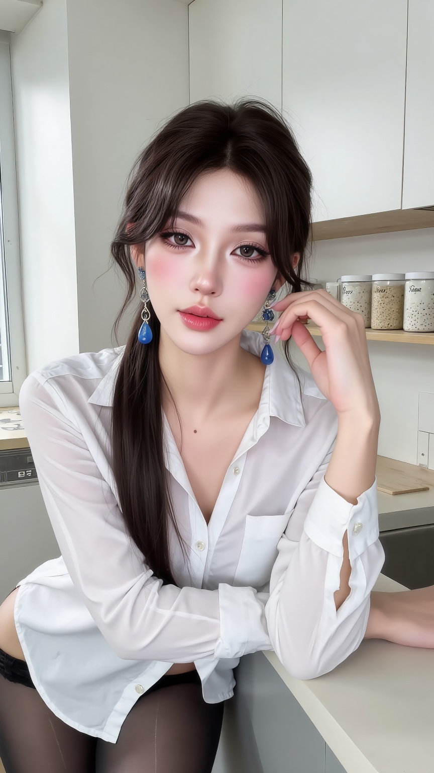 Photograph of an East Asian woman with fair skin and long,dark brown hair in a side ponytail,leaning forward on a kitchen counter. She wears a white,long-sleeved,button-up shirt that is slightly unbuttoned,revealing a hint of black underwear,and black sheer pantyhose. Her left hand rests on the counter while her right hand touches her cheek. She has pink blush on her cheeks,dark eyeliner,and wears large,dangling blue earrings. The background includes a modern,minimalist kitchen with white cabinets,a window on the left,and shelves with small,labeled containers. The lighting is natural,coming from the window.,