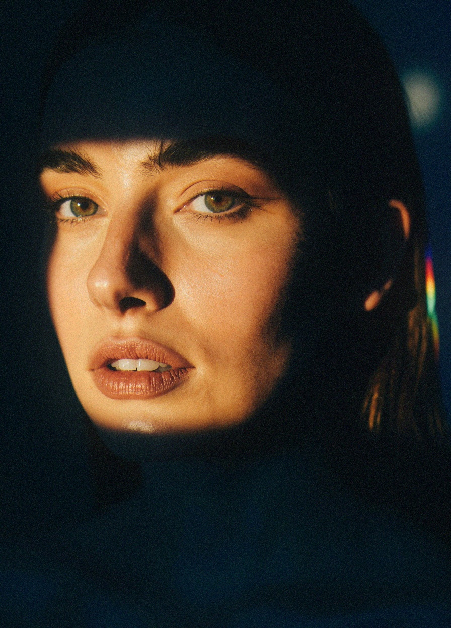 The image is a high-resolution photograph of a young woman's face,  capturing her in a dramatic,  artistic light. She is a...