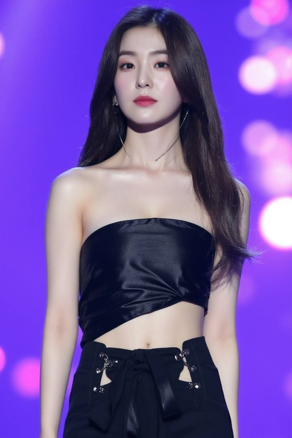 The image shows a young korean woman singing on stage. She has long,  dark hair and is wearing a fitted,  strapless black...