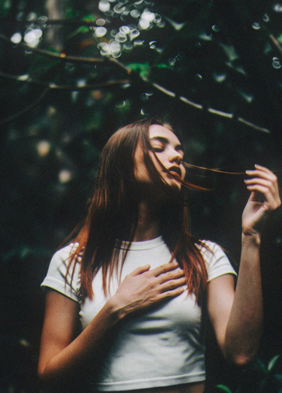 The image is a photograph featuring a young woman with a striking,  ethereal quality,  likely taken in a forest or wooded...