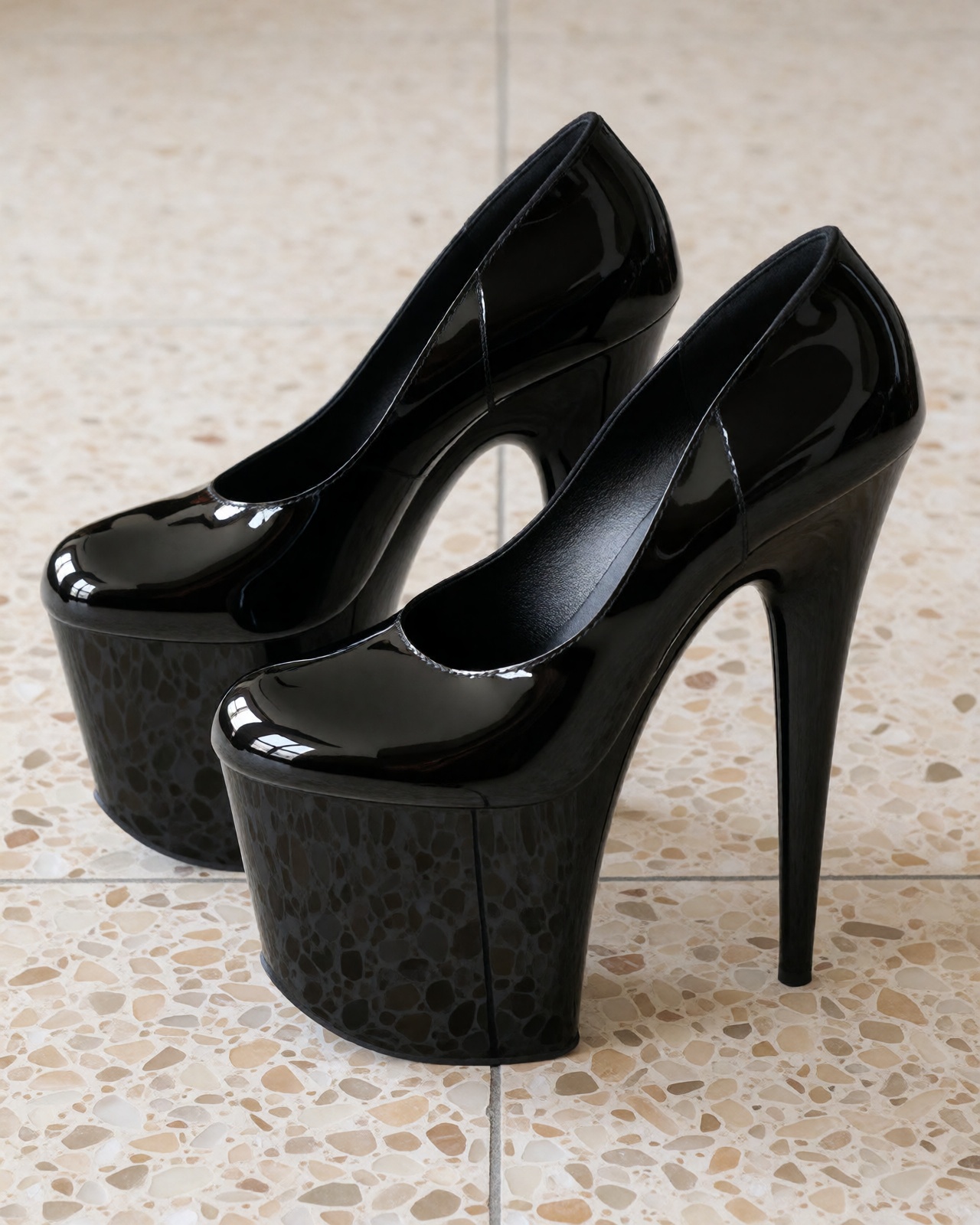 A detailed product photograph of all-black glossy patent Pleasers Flamingo extreme platform heels centered on speckled bei...