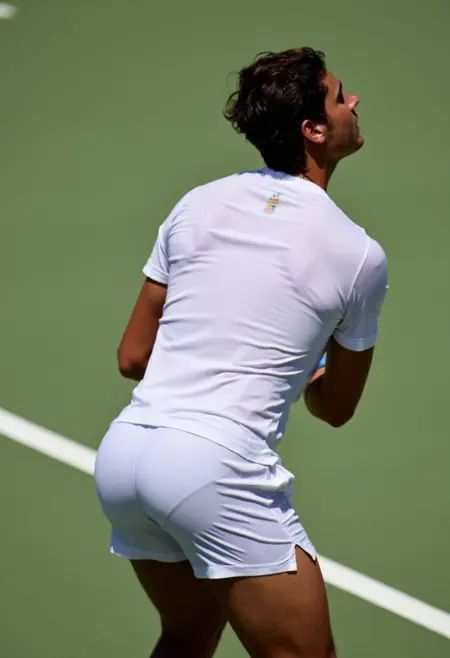 Photo of a Brazilian tennis player standing on a sunlit tennis court,  captured from behind just as he prepares to serve....
