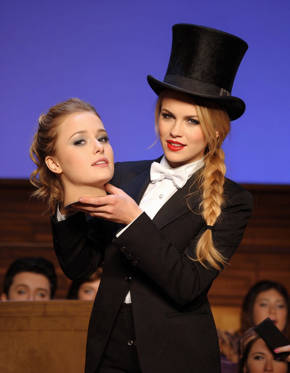 This is a far shot photograph of a female magician in a tuxedo and top hat holding a beautiful young woman's disembodied h...