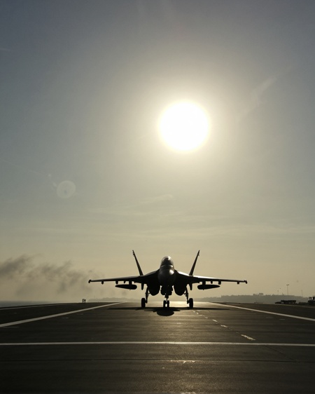 view over airfield on air carrier on sea, foggy cloud deep, silhouette of f18 hornet coming down