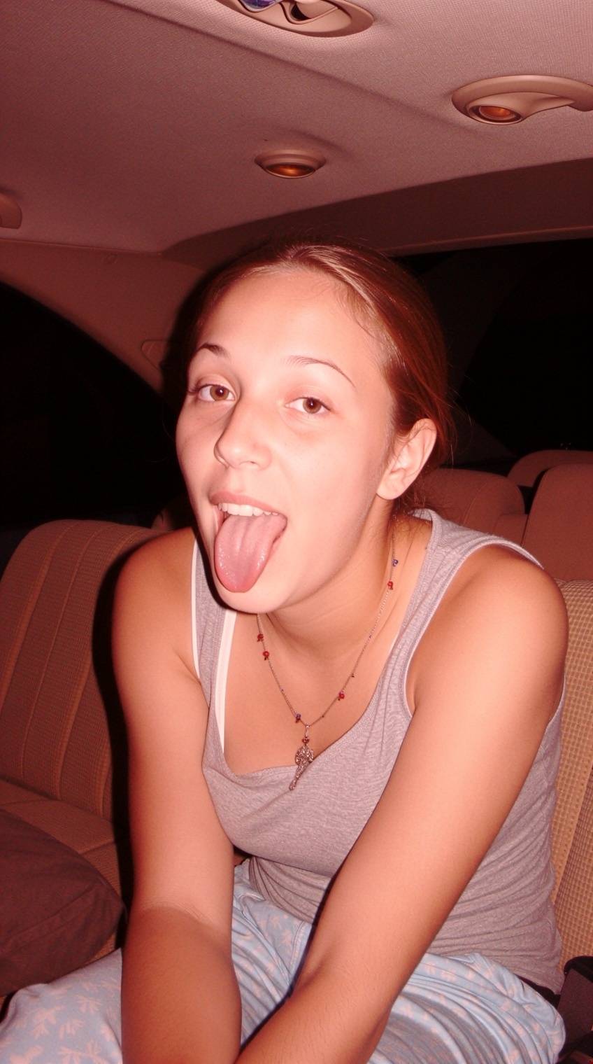 a young woman with light brown hair pulled back sits on a textured,  quilted bench inside a dimly lit vehicle,  likely a b...