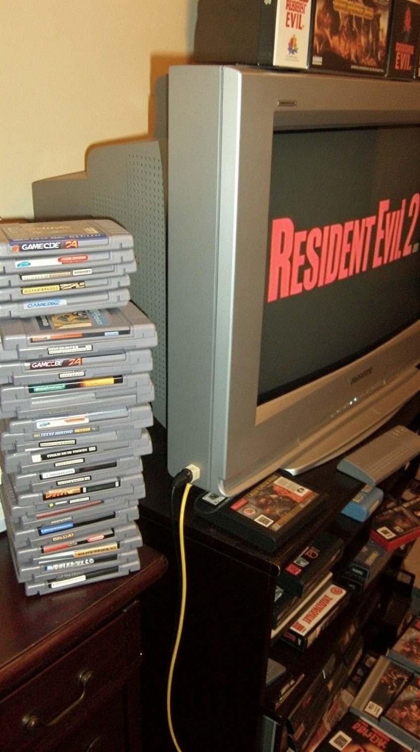 a cluttered entertainment setup features a stack of gray game cartridges,  primarily from the nintendo 64 and gamecube,  a...