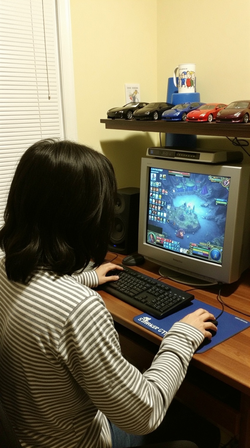 a person with shoulder-length dark hair sits at a wooden desk,  facing a crt monitor displaying a fantasy-themed video gam...