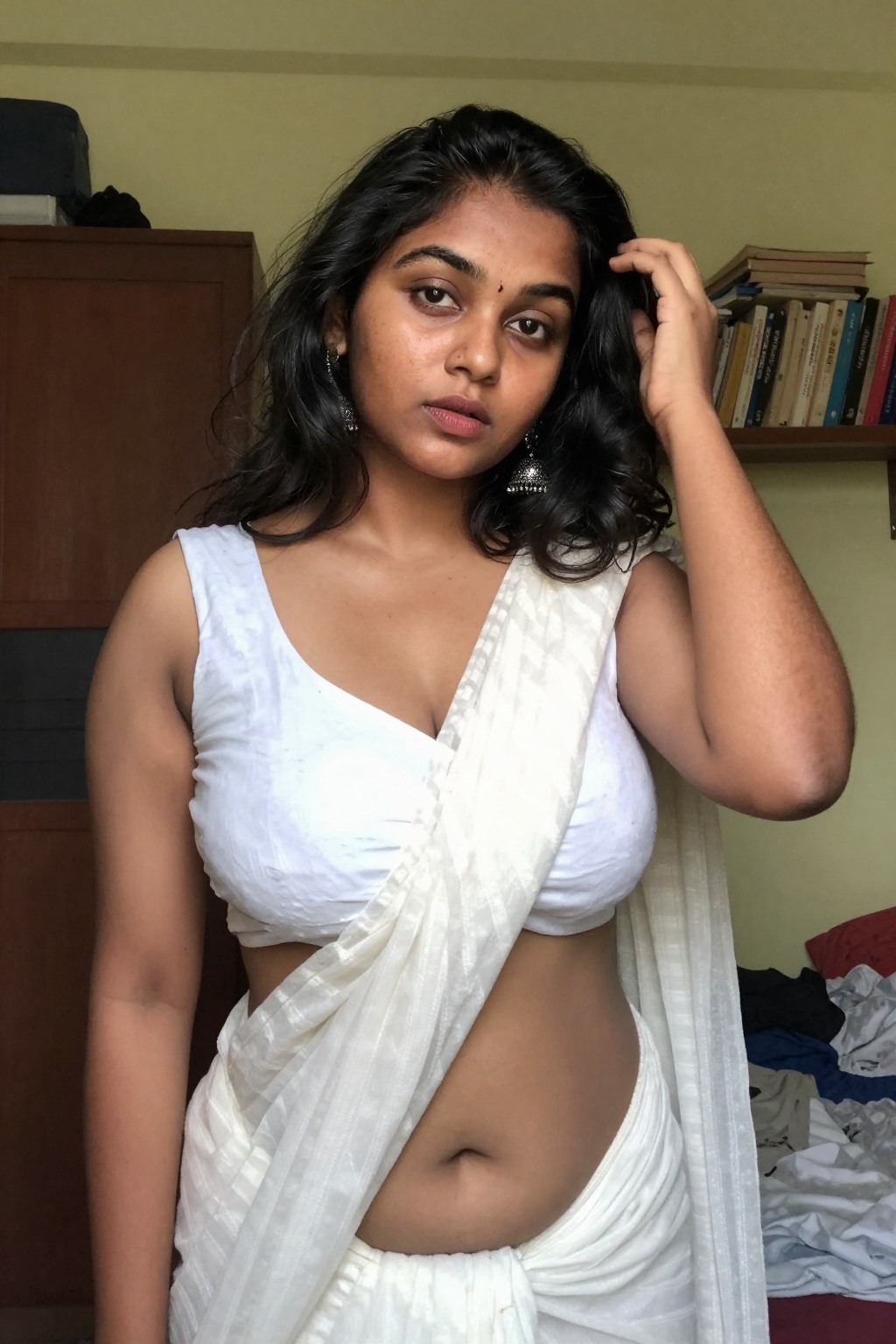 Photograph of a young South Asian woman with medium brown skin and shoulder-length wavy black hair,  standing in a modestl...