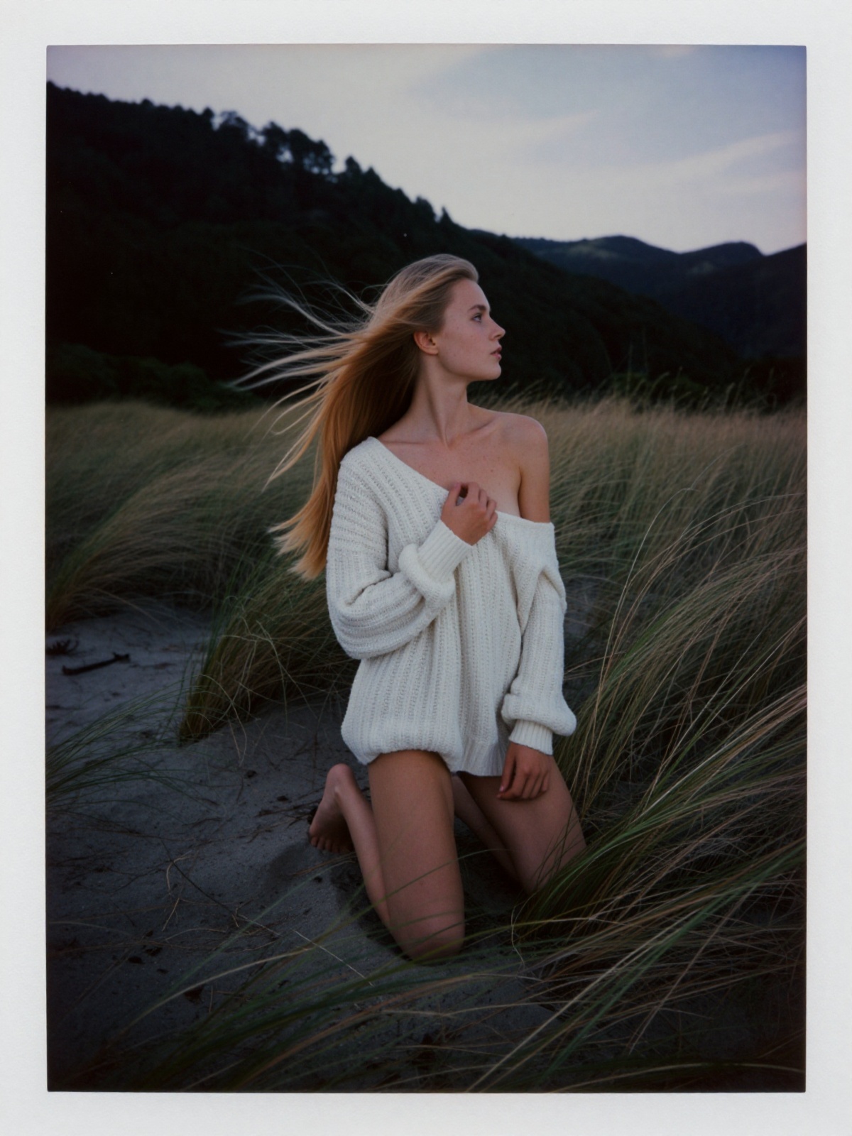 An authentic ******* analogue photograph of a young woman in her early twenties kneeling in windswept coastal dune grass a...