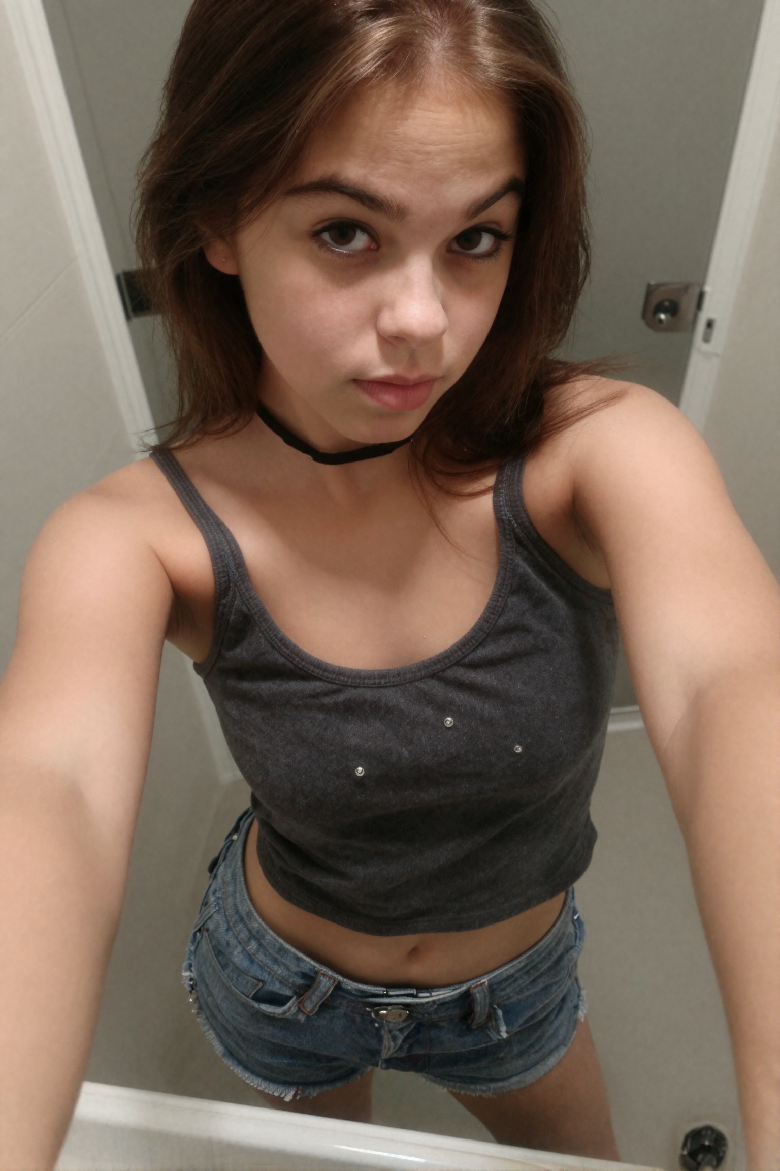 Create a candid photograph of a 16-year-old teenage girl,  capturing her in a moment of taking a selfie in a bathroom. The...