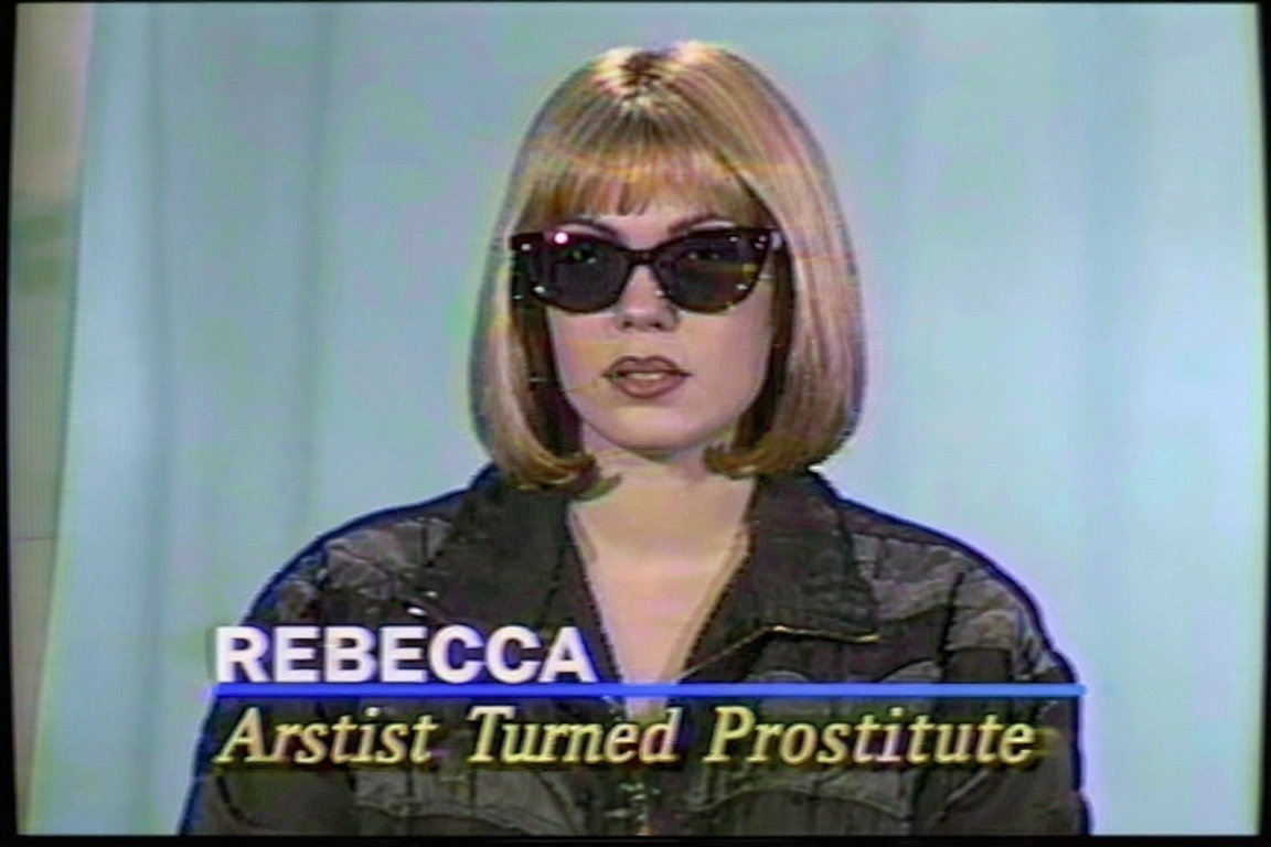 A television screen capture from a retro broadcast features a woman against a soft,  light blue studio backdrop. She has a...