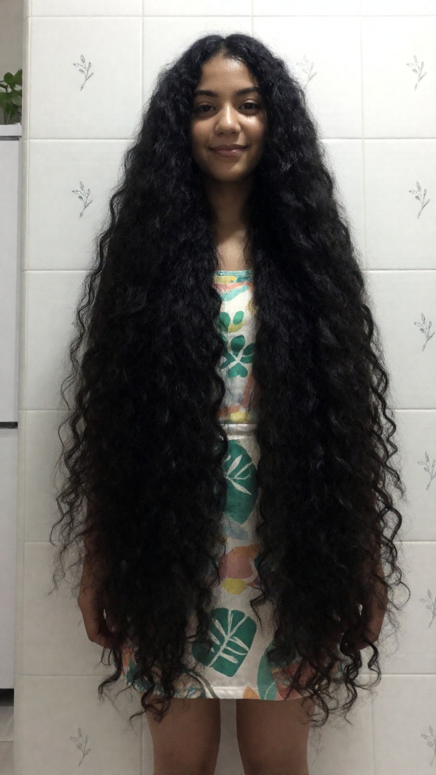 Photograph of a young woman standing in a tiled bathroom. She has long very thick and extremely curly black hair that casc...