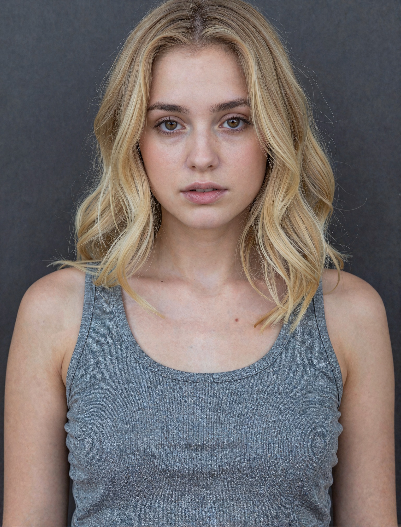 The image is a portrait of a young woman with shoulder-length blonde hair. She is wearing a gray **** top and is standing...