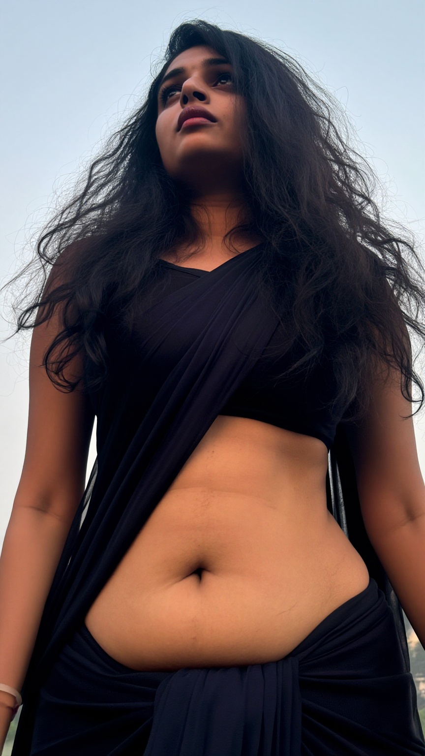A worm’s-eye view low-angle shot captures a Mallu young slim woman with a seductive expression. Her long,  wavy hair casca...