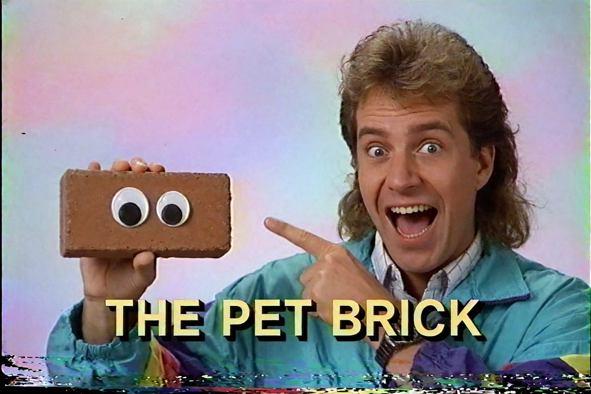 A 1990s VHS screenshot of a cheesy late-night infomercial. A salesman with a big mullet hairstyle and a bright teal windbr...