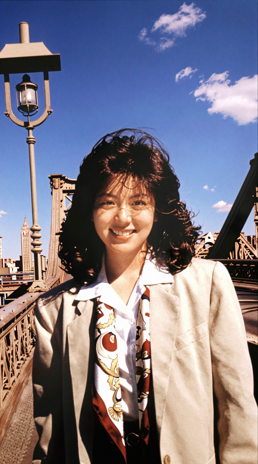 @showa_idol,  A woman with shoulder-length dark wavy hair smiles warmly at the camera,  standing on a metal pedestrian wal...