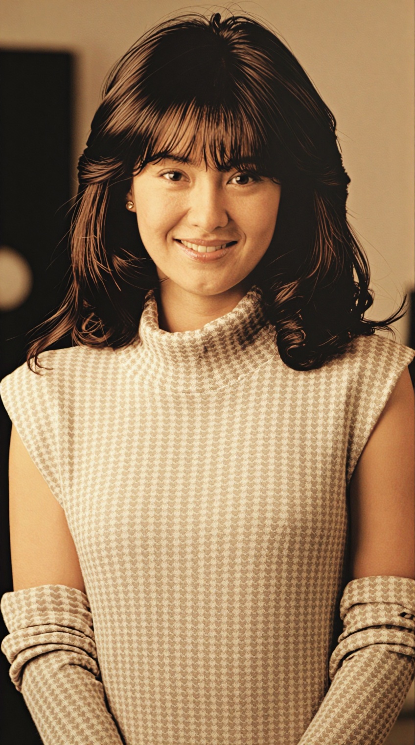 A woman with shoulder-length dark brown hair and bangs smiles softly at the camera,  her expression warm and gentle. She w...