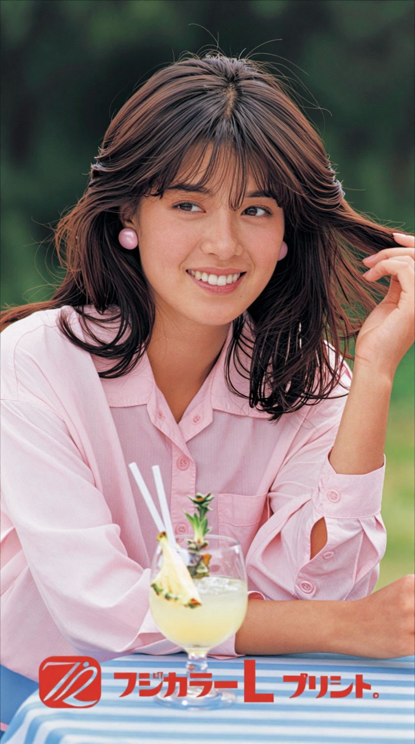 A young woman with shoulder-length brown hair and bangs smiles warmly at the camera,  her right hand gently lifting a stra...