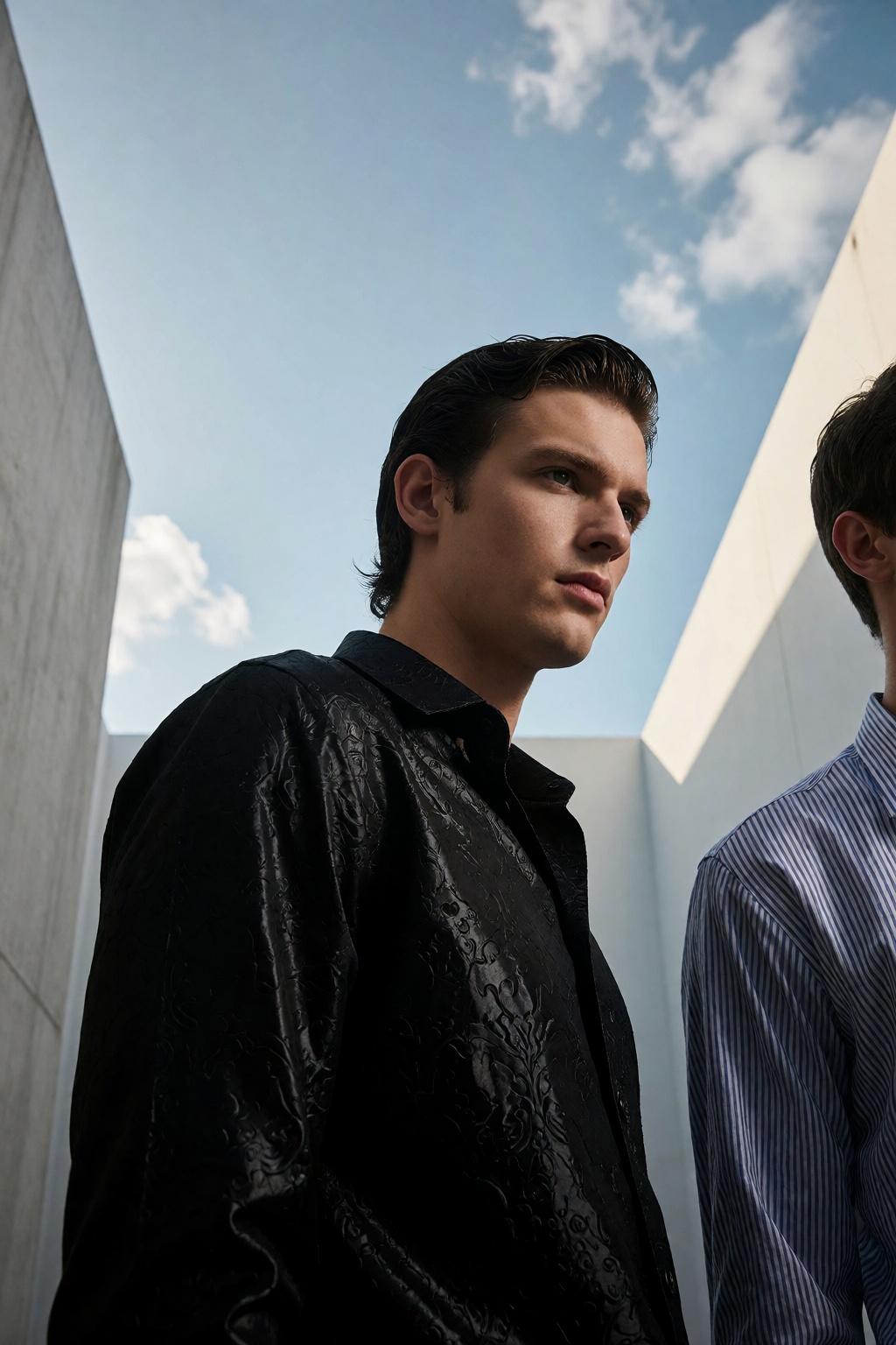 A high-end fashion editorial low-angle photo captures two handsome young men outdoors,  their forms sharply defined agains...
