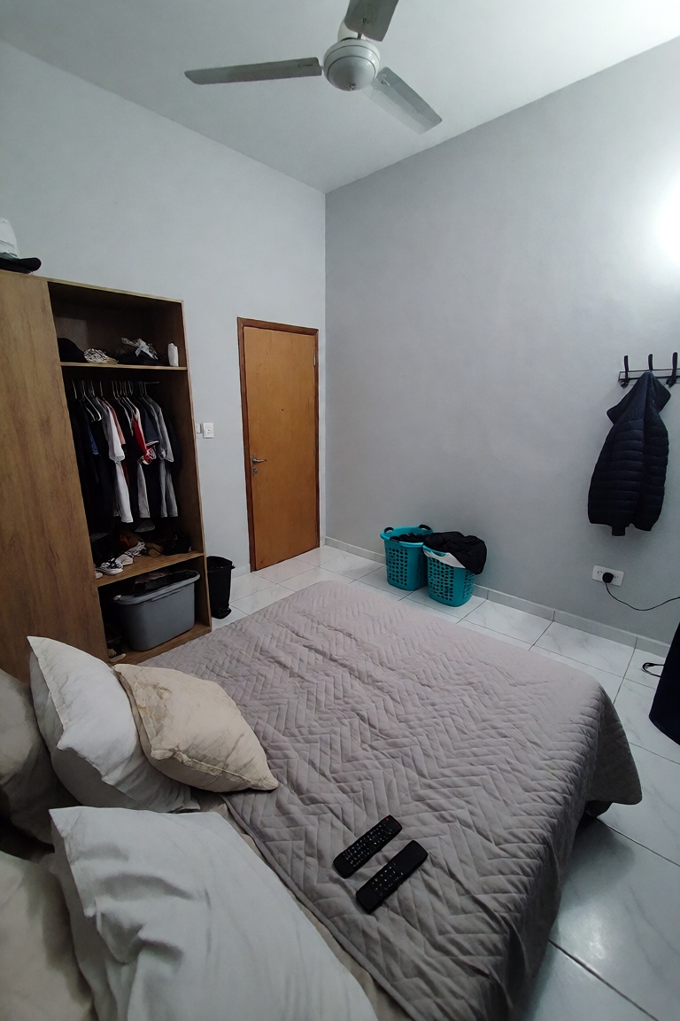 A high-angle interior shot of a minimalist,  sparsely furnished bedroom with light gray walls and white tiled flooring. In...