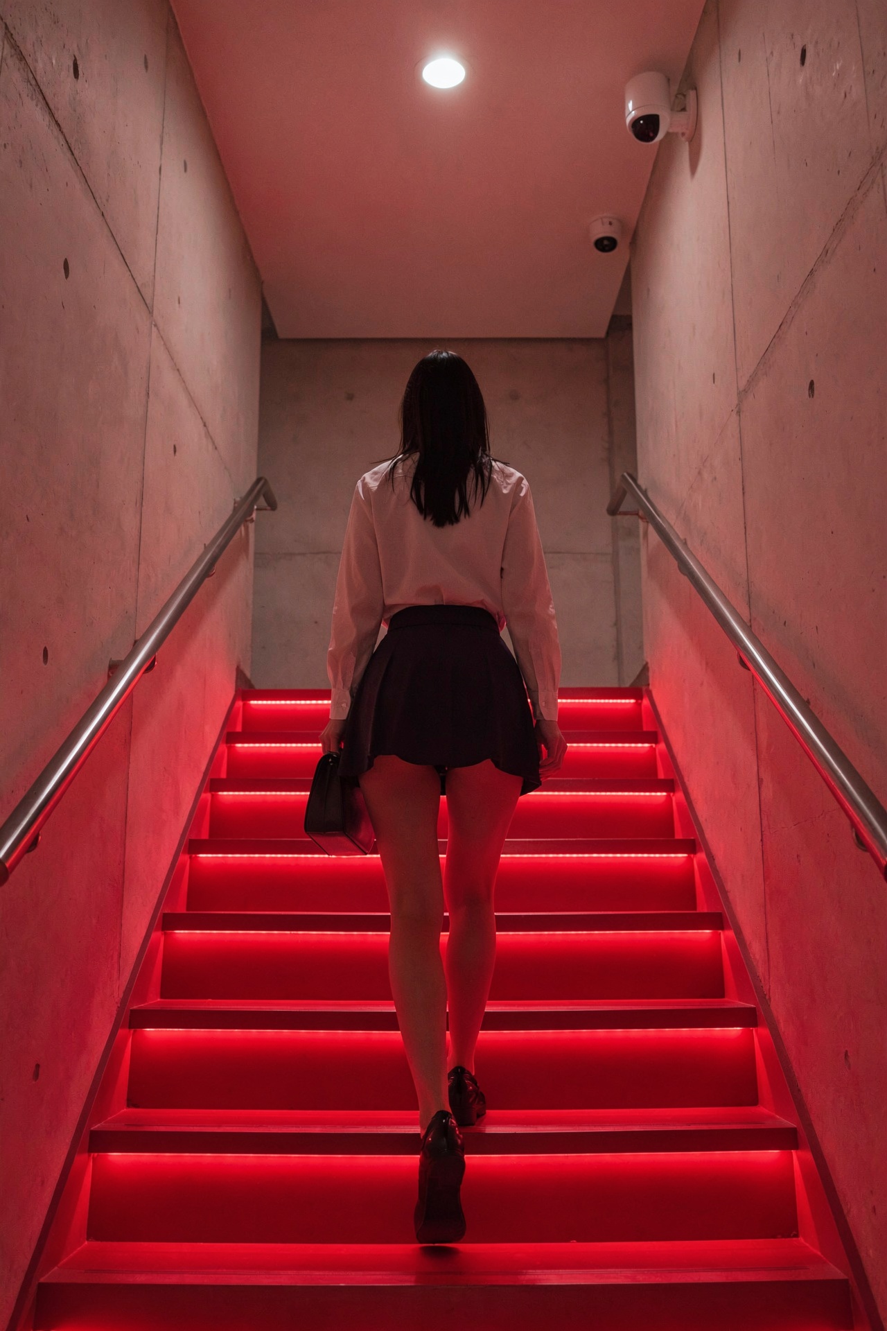 rear view of a person climbing a brightly red lit staircase. the individual has dark hair and is wearing a dark ultra mini...