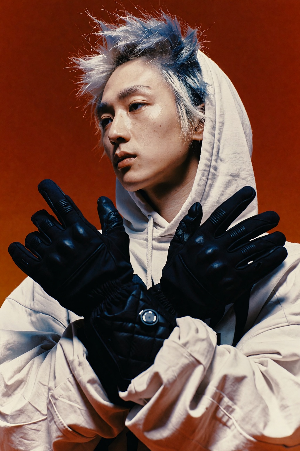 Editorial fashion photograph of a young East Asian man with tousled ash-blue and silver-streaked spiky hair,  strands catc...
