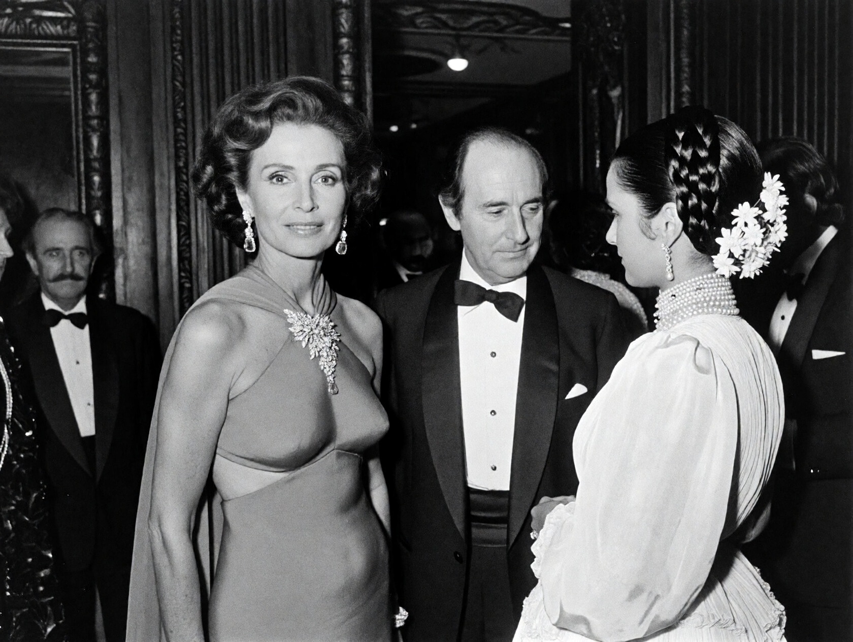 {"high_level_description":"A grain-heavy,  black and white candid photograph from a 1970s high-society gala. Three elegant...