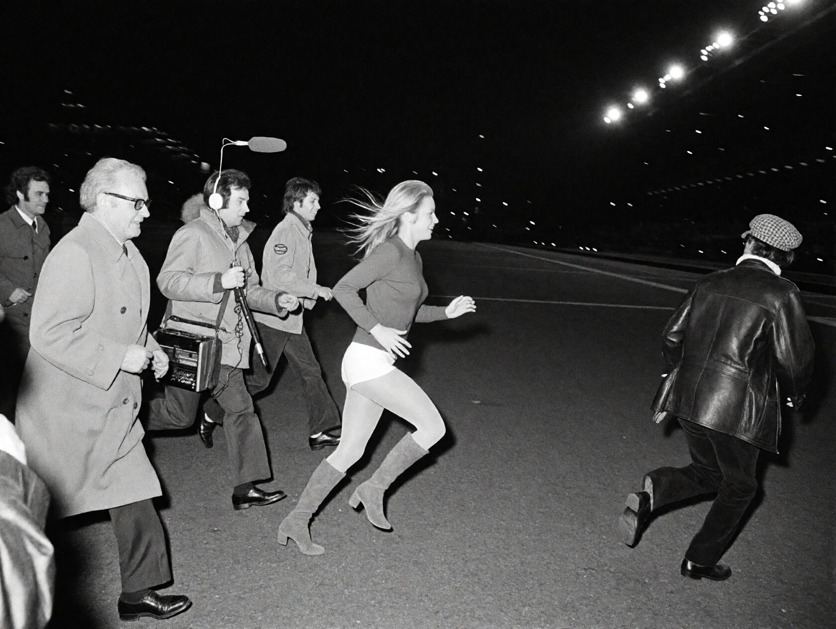 {"high_level_description":"A grain-heavy 1970s black and white photograph captures a blonde woman in mid-stride,  fleeing...
