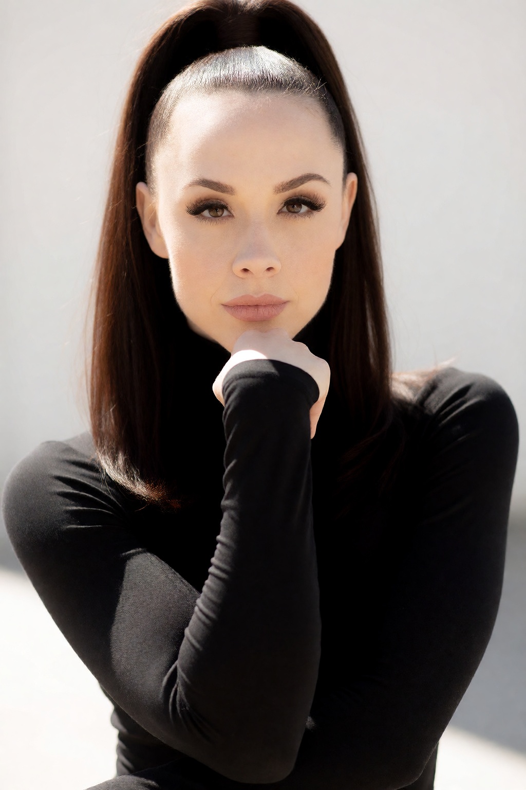 A high-fashion head and shoulders portrait of woCh40n with dark,  straight hair styled into a high ponytail. She rests her...