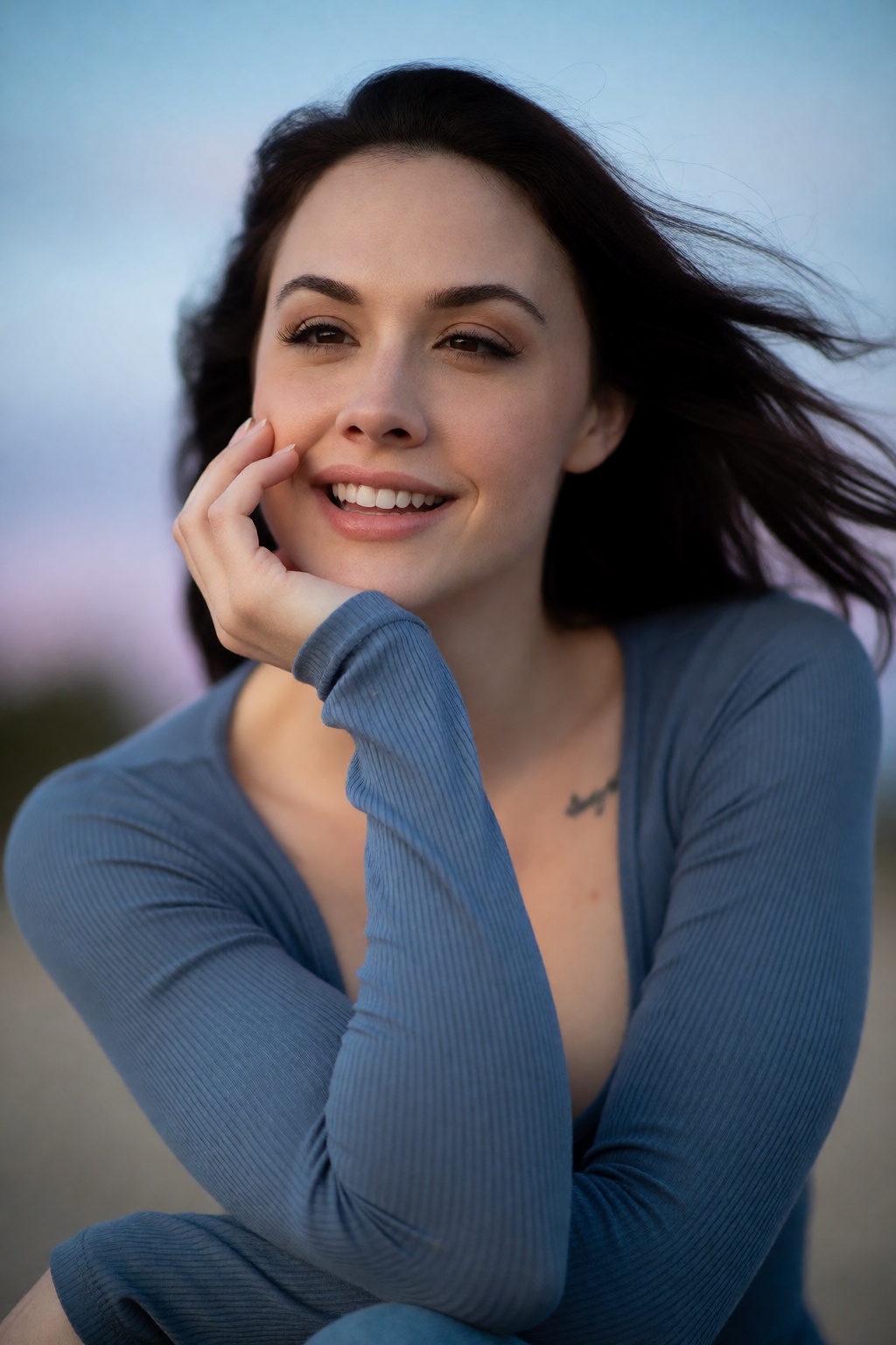 A candid,  relaxed head and shoulders portrait of woCh40n with dark hair blowing softly in a mild breeze. She rests her ch...