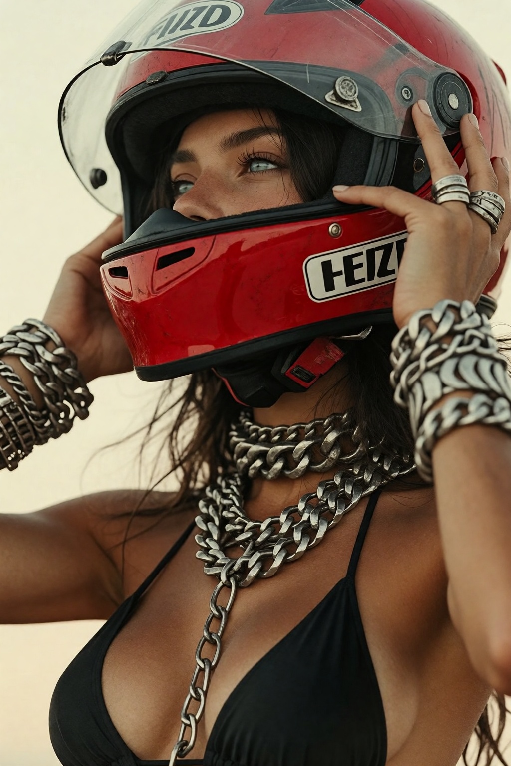 Low-angle,  close-up of a young woman with tanned skin and dark hair taking off a bright red motorcycle racing helmet. She...