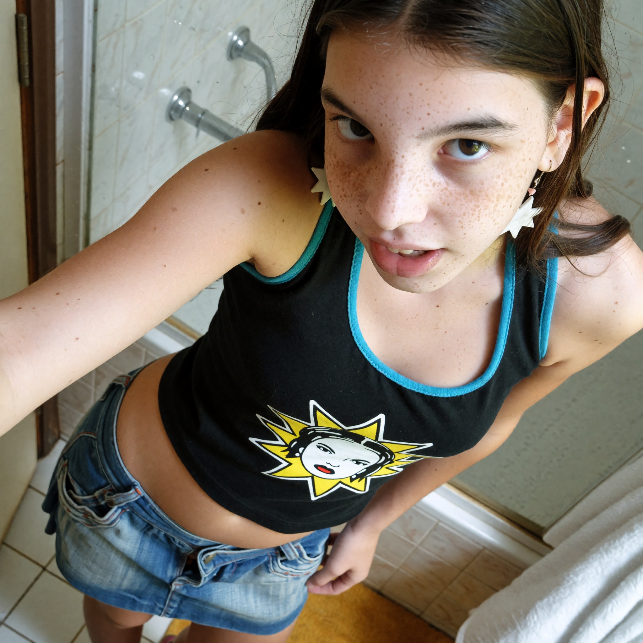 Create a candid photograph of a freckled 16-year-old teenage girl,  capturing her in a moment of taking a selfie in a bath...