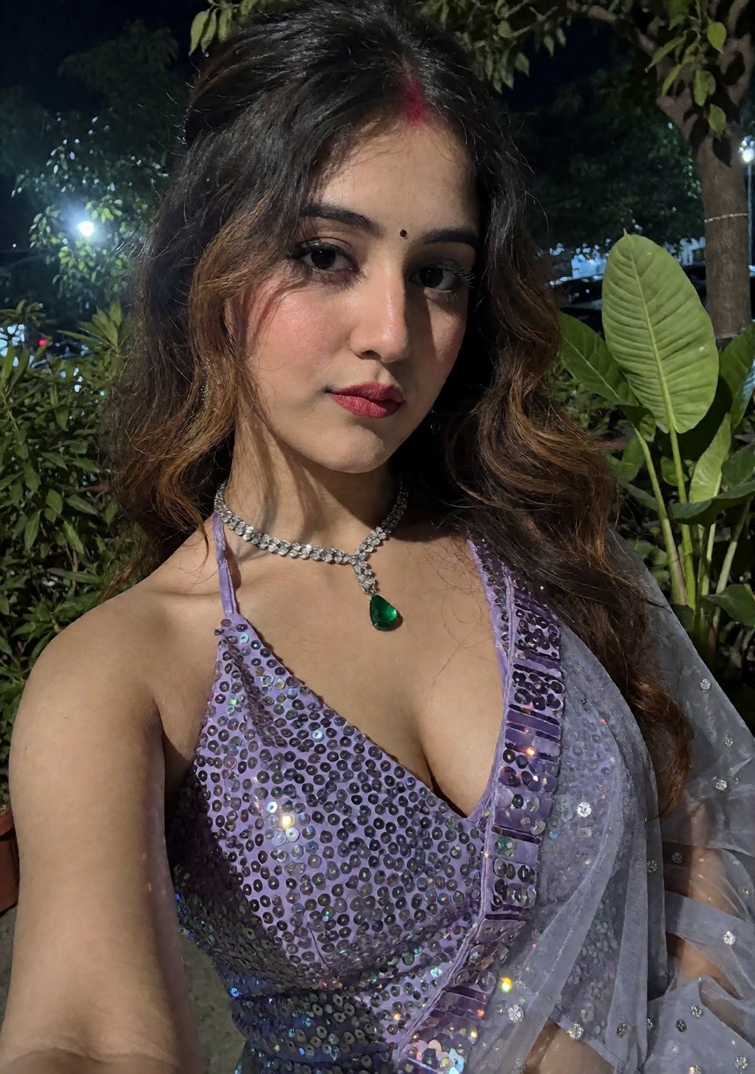 A Selfie of an indian woman wearing a sparkly,  halter-style dress with a deep neckline. The dress is light purple and app...