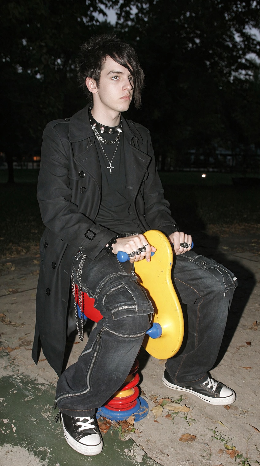 @2000s_core,  A young man dressed in full goth attire,  including a black trench coat and baggy pants with many zippers an...