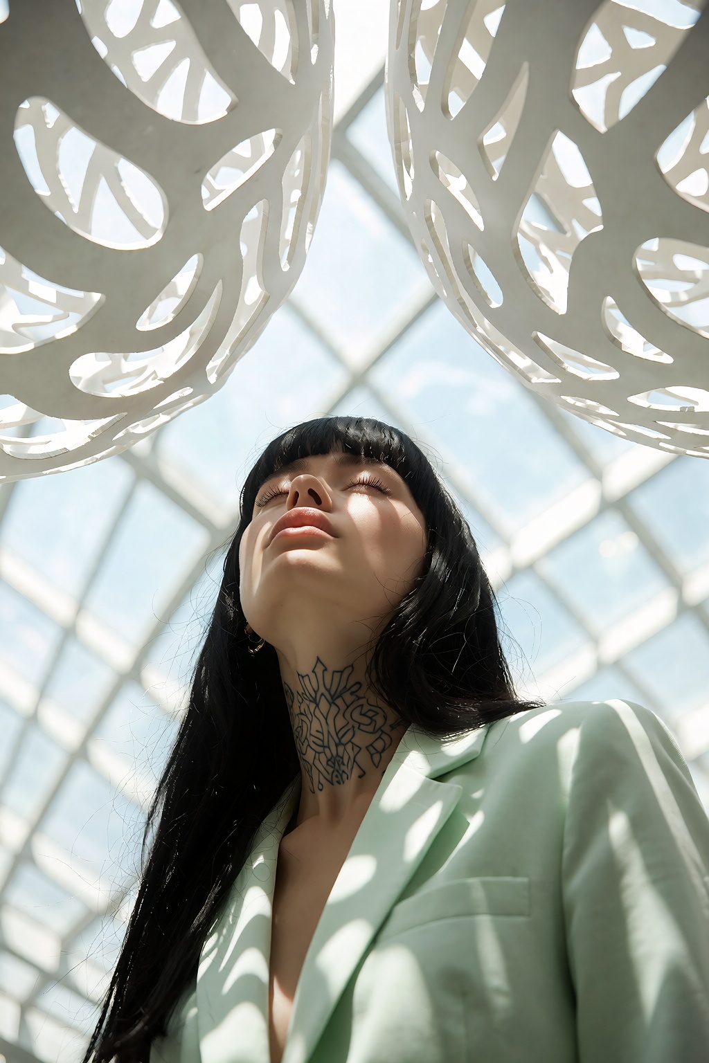 A woman with long black bangs and a neck tattoo tilts her head back with closed eyes,  wearing a pale green blazer. Bright...
