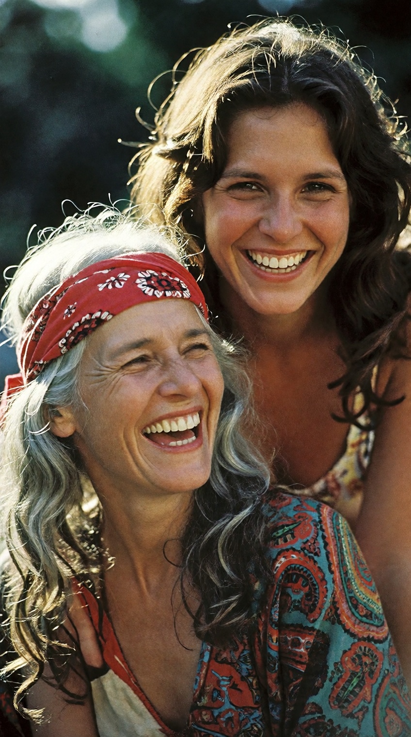 A candid,  heartwarming 1970s vintage portrait of two free-spirited bohemian women sharing a joyful moment outdoors. In th...