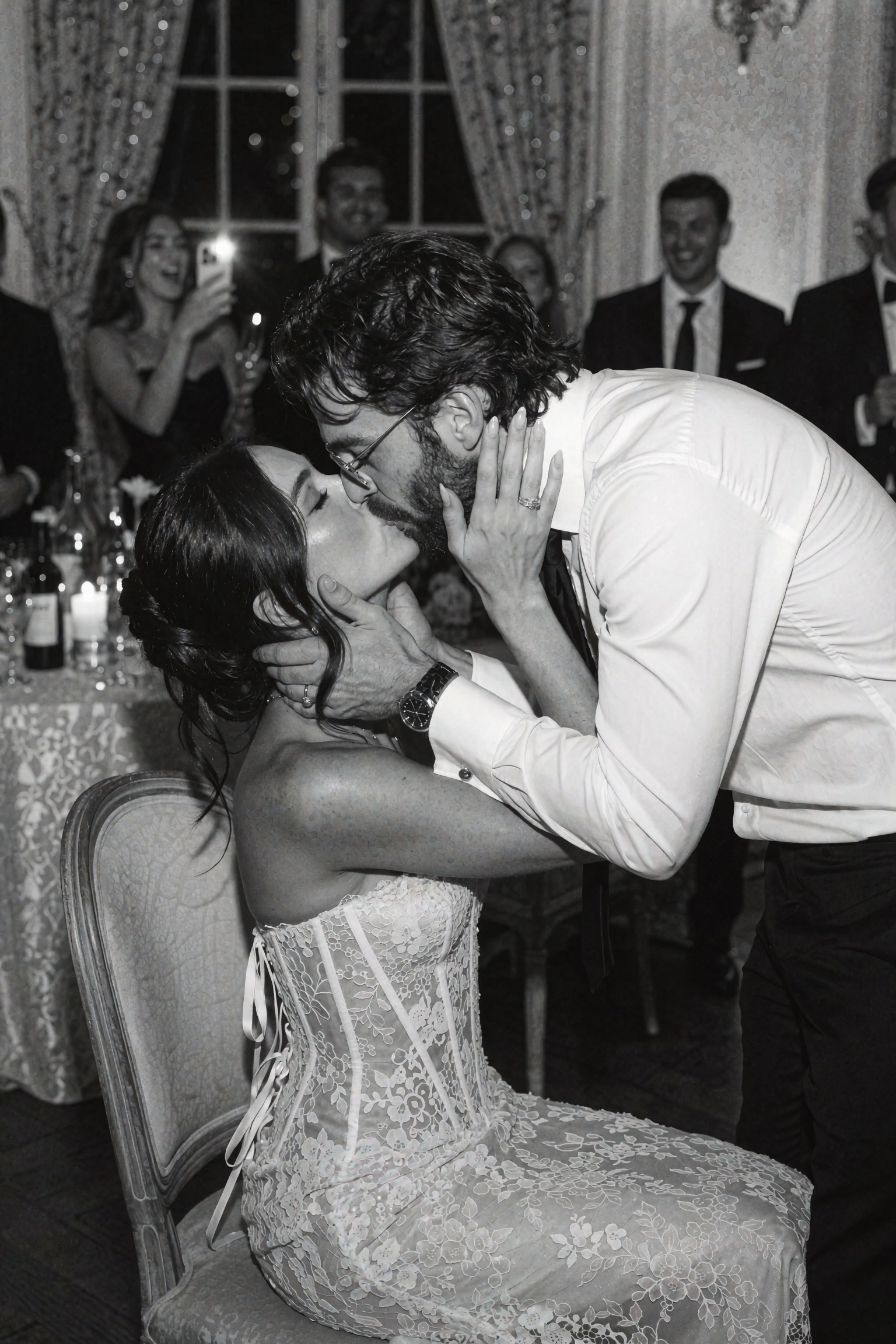 Cinematic black-and-white editorial photograph of a couple sharing a passionate kiss at an elegant evening reception,  the...