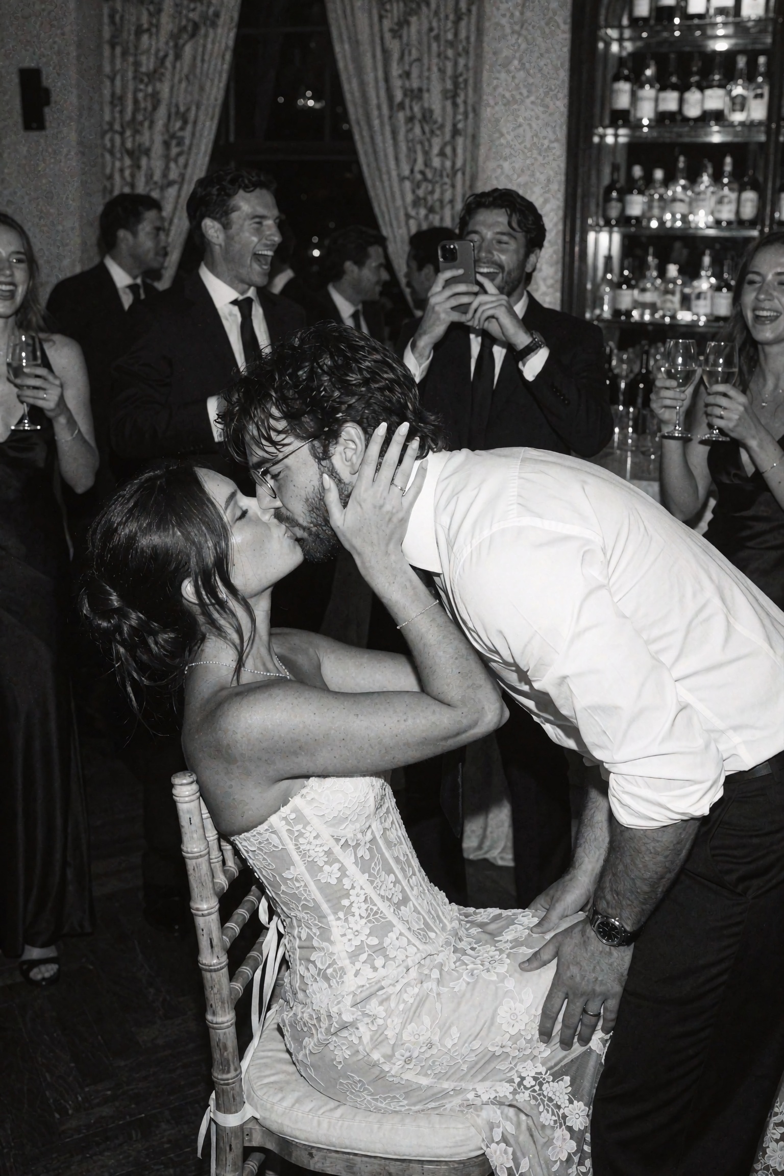 Candid documentary-style UGC flash snapshot of a young couple kissing at a lively indoor party reception,  the woman seate...