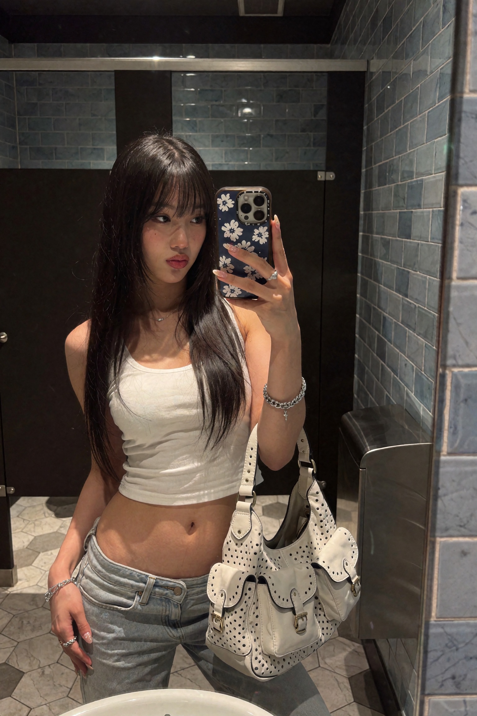 Candid UGC smartphone mirror selfie of a young woman in a dim tiled restroom,  head turned slightly to the side with lips...