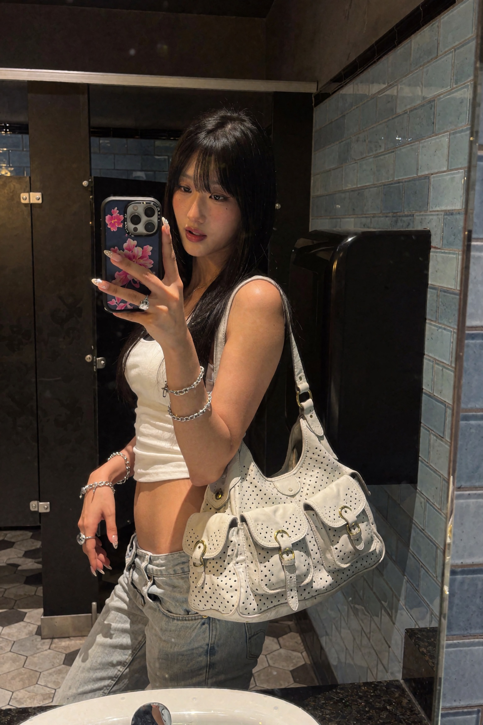 Candid UGC smartphone mirror selfie of a young woman in a dim tiled restroom,  head turned slightly to the side with lips...