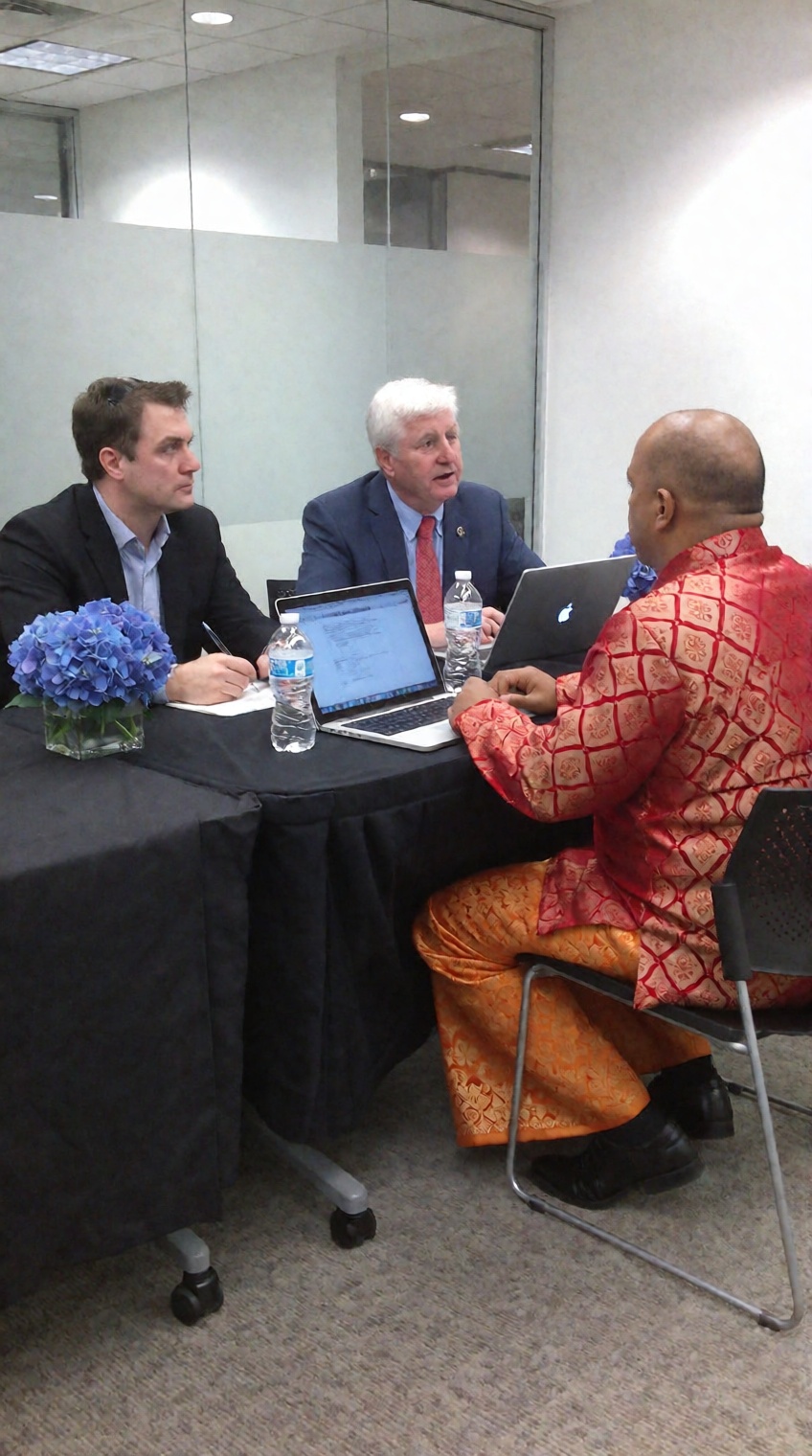 a photo taken by phone,  Three men sitting at a conference table with laptops and water bottles,  in a modern office setti...