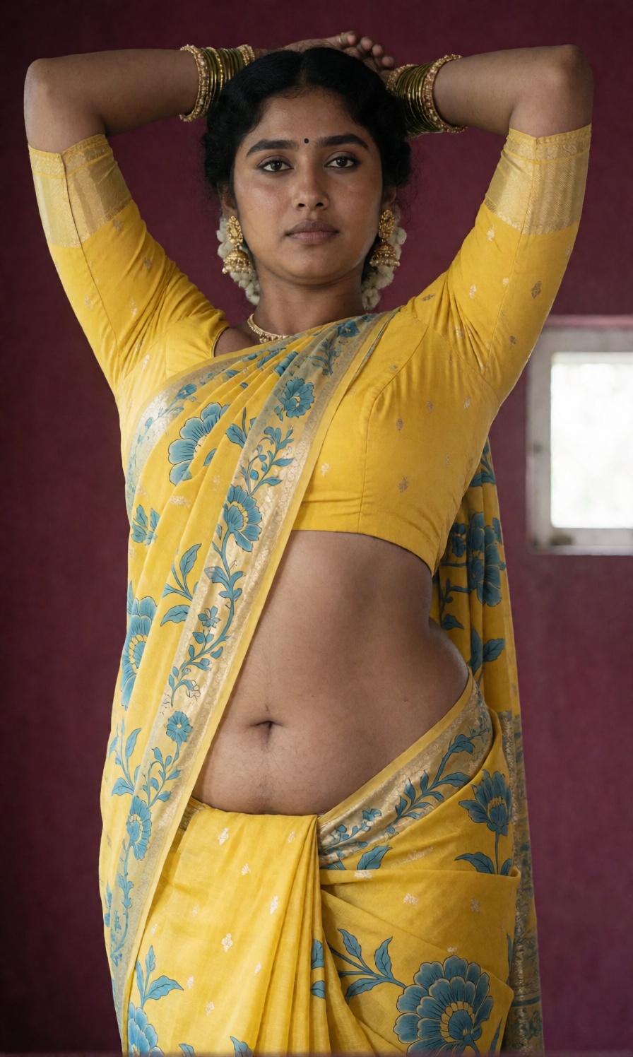 Photograph of an Indian woman standing against a maroon background. She has dark brown skin and dark hair,  styled in an u...
