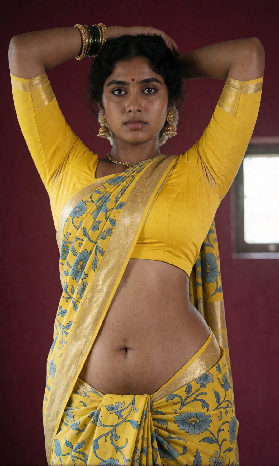 Photograph of an Indian woman standing against a maroon background. She has dark brown skin and dark hair,  styled in an u...
