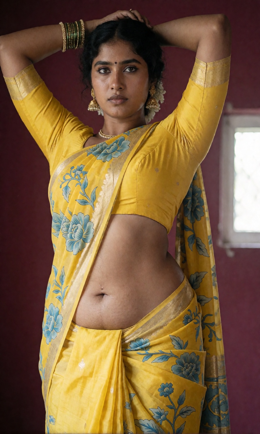 Photograph of an Indian woman standing against a maroon background. She has dark brown skin and dark hair,  styled in an u...