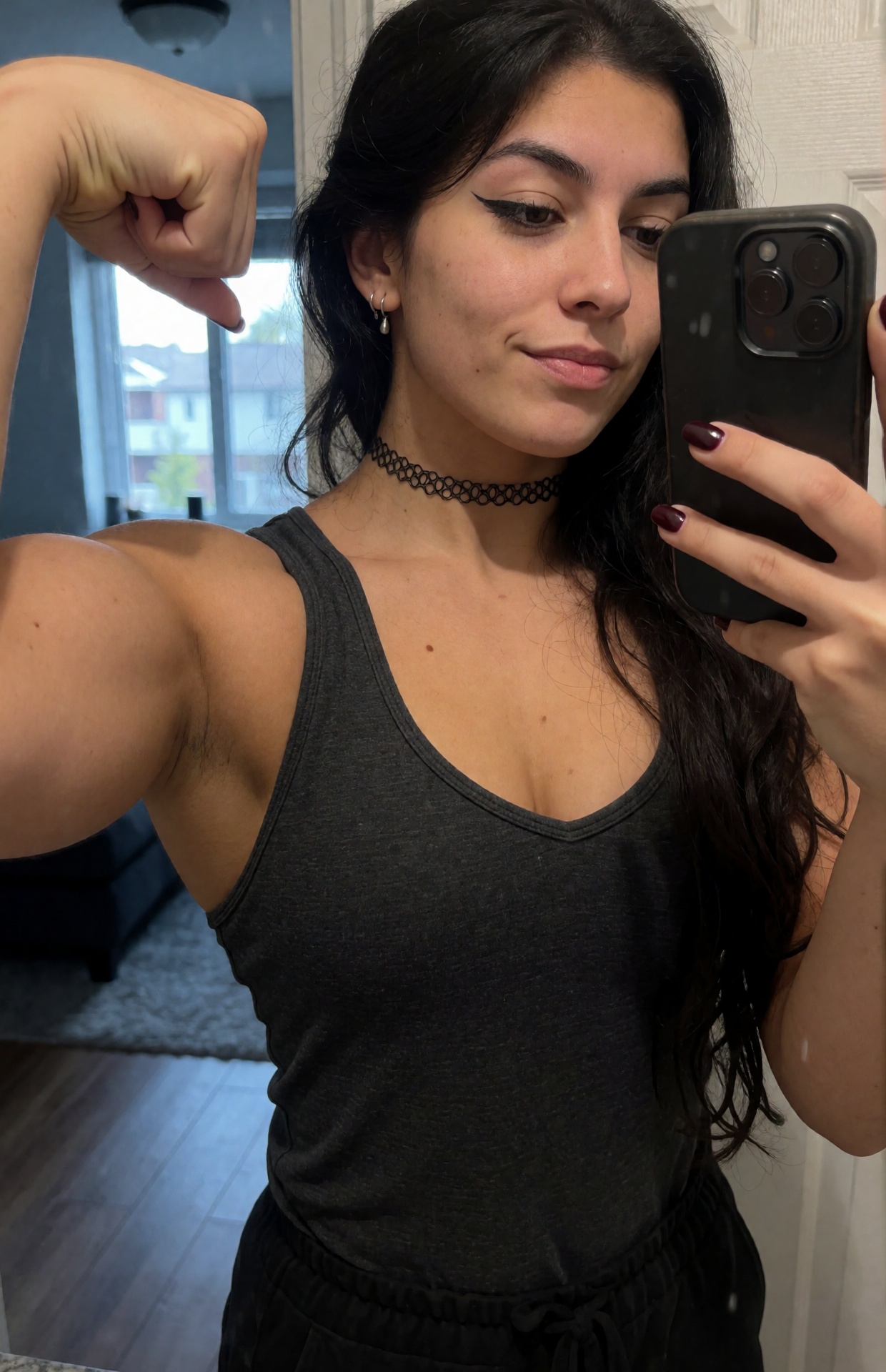 Your favorite goth muscle mommy takes a close-up mirror selfie in a softly lit apartment bathroom,  a voluptuous slightly...
